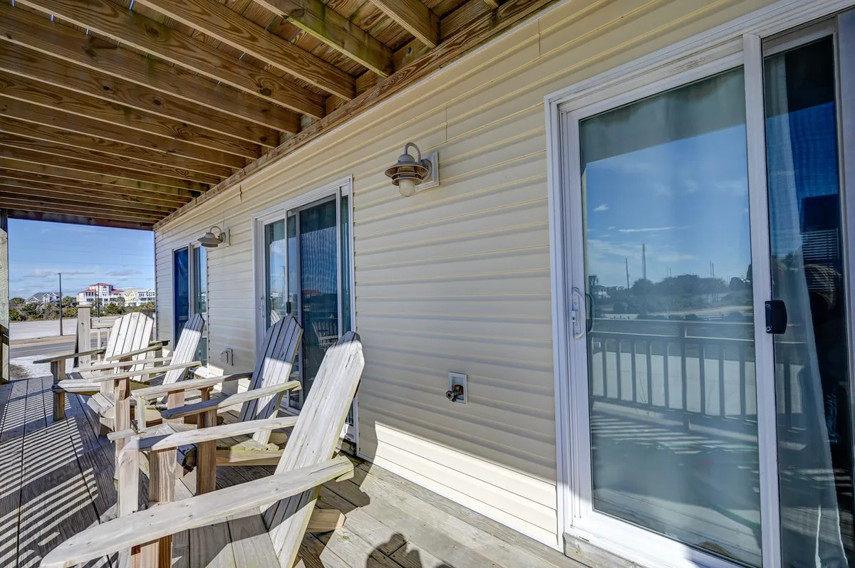 A welcoming exterior scene featuring sturdy wooden chairs arranged on a sun-kissed patio near sliding glass doors. The area is designed for casual relaxation, socializing, and enjoying the ocean breeze from sunrise to starry nights.