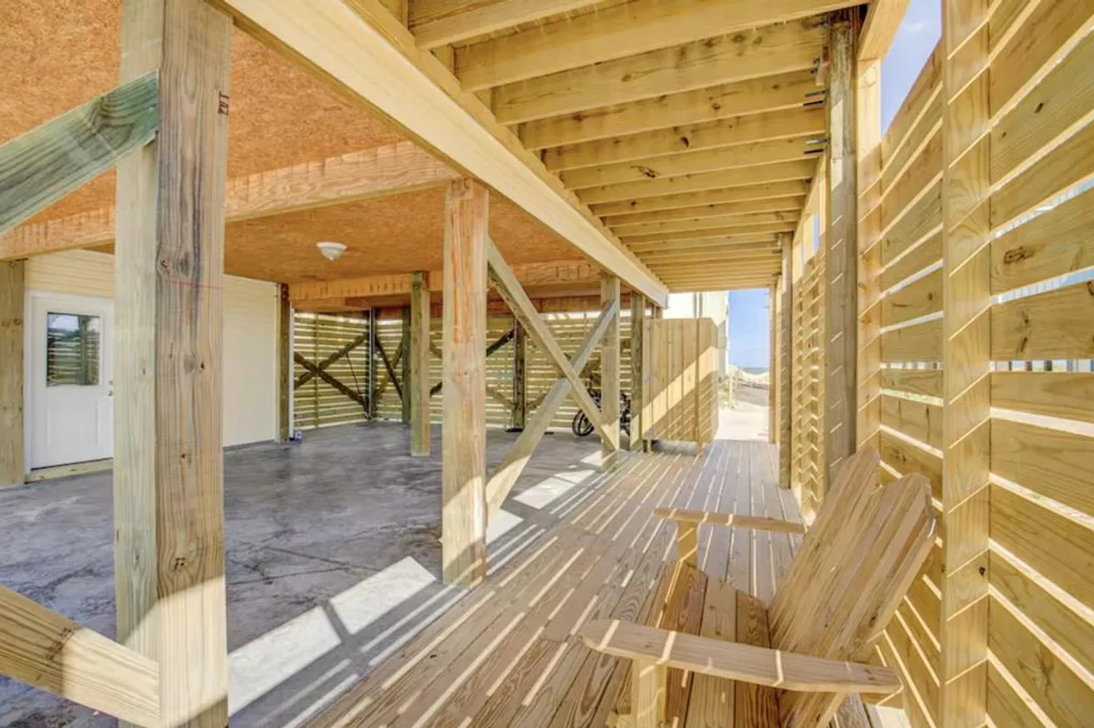Featuring a sun-drenched wooden deck with inviting Adirondack chairs and sturdy wooden beams, this exterior shot exemplifies open space for relaxation and gatherings. The open layout and tranquil setting evoke a sense of peacefulness and a spot well-suited for stargazing or afternoon lounging.